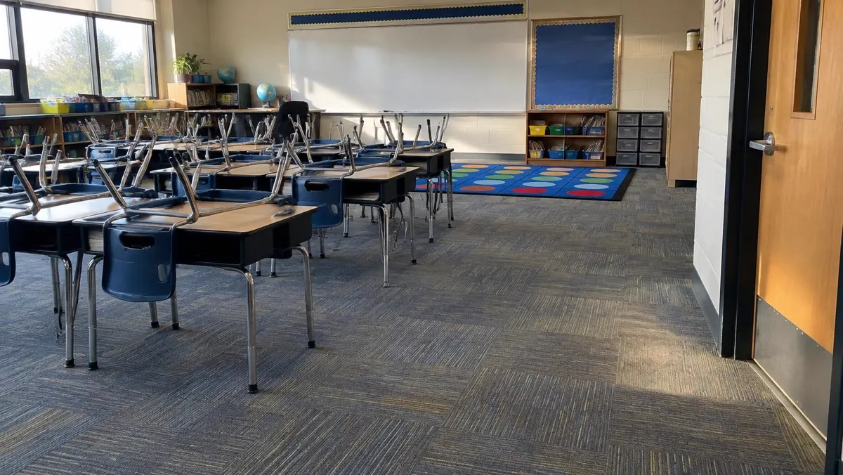 Empty classroom with carpet tile, desks and chairs stacked after school