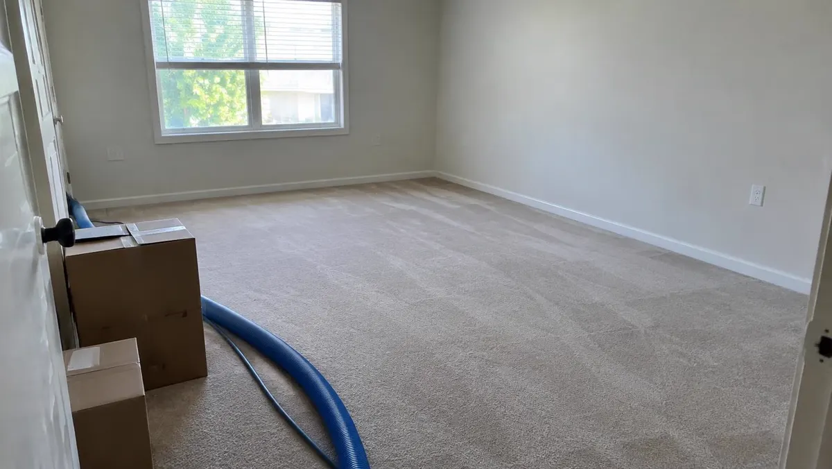 Empty apartment bedroom with carpet, moving boxes and an extraction hose at the doorway